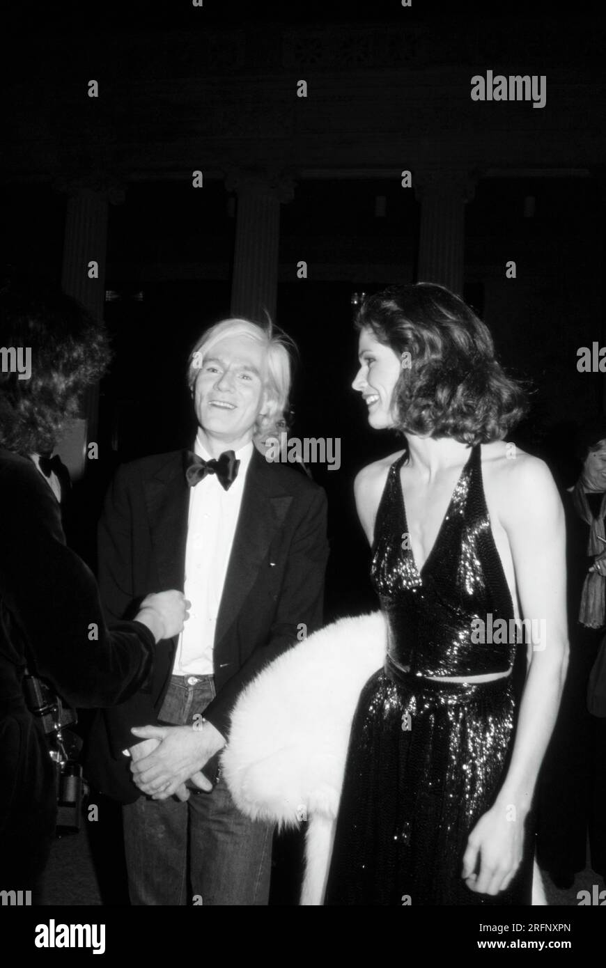 Andy Warhol with unidentified woman in evening gown in 1977. Warhol was an American visual artist, film director, producer, and leading figure in the pop art movement. His works explore the relationship between artistic expression, advertising, and celebrity culture that flourished by the 1960s, and span a variety of media, including painting, silkscreening, photography, film, and sculpture. Some of his best-known works include the silkscreen paintings Campbell's Soup Cans  and Marilyn Diptych. Photo by Bernard Gotfryd Stock Photo