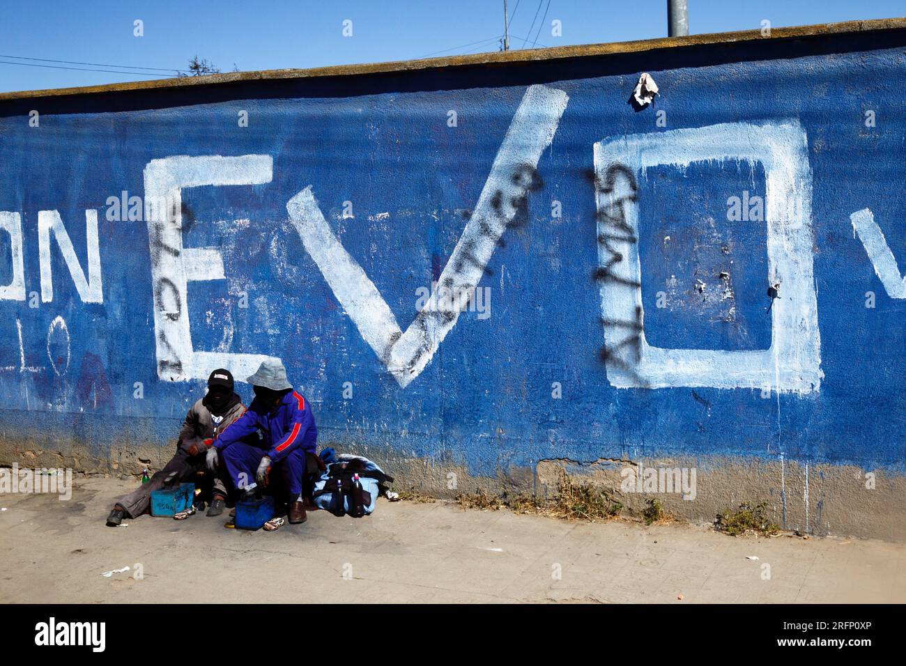 Shoeshiners sitting in front of Evo Morales 2014 presidential elections propaganda on wall, El Alto, Bolivia Stock Photo