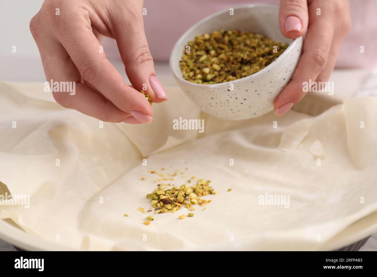 Woman putting filling into baking dish with dough to prepare baklava, closeup Stock Photo