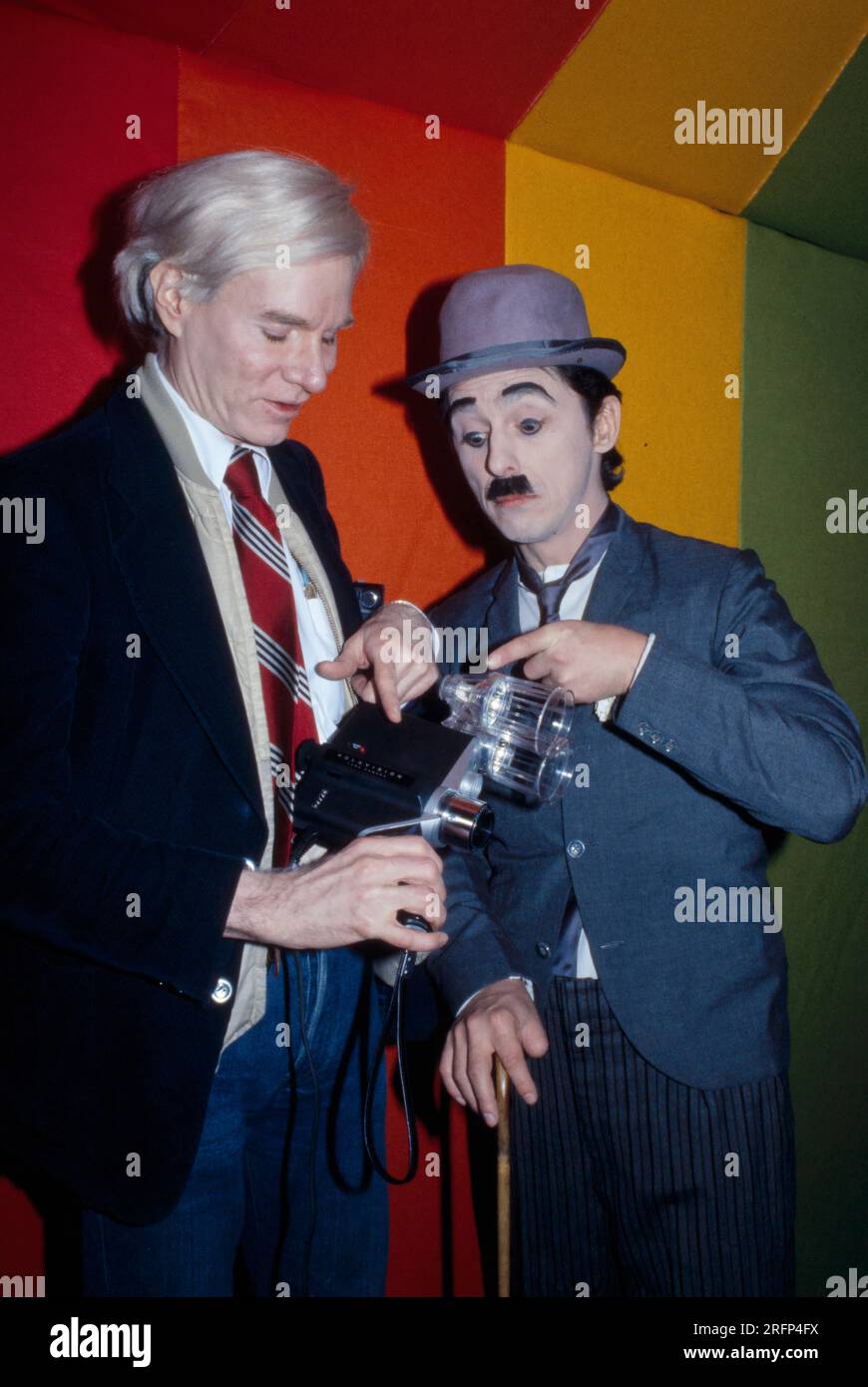 Andy Warhol with new Polaroid Polavision movie camera at an art opening in 1977. Warhol was an American visual artist, film director, producer, and leading figure in the pop art movement. His works explore the relationship between artistic expression, advertising, and celebrity culture that flourished by the 1960s, and span a variety of media, including painting, silkscreening, photography, film, and sculpture. Some of his best-known works include the silkscreen paintings Campbell's Soup Cans  and Marilyn Diptych. Photo by Bernard Gotfryd Stock Photo