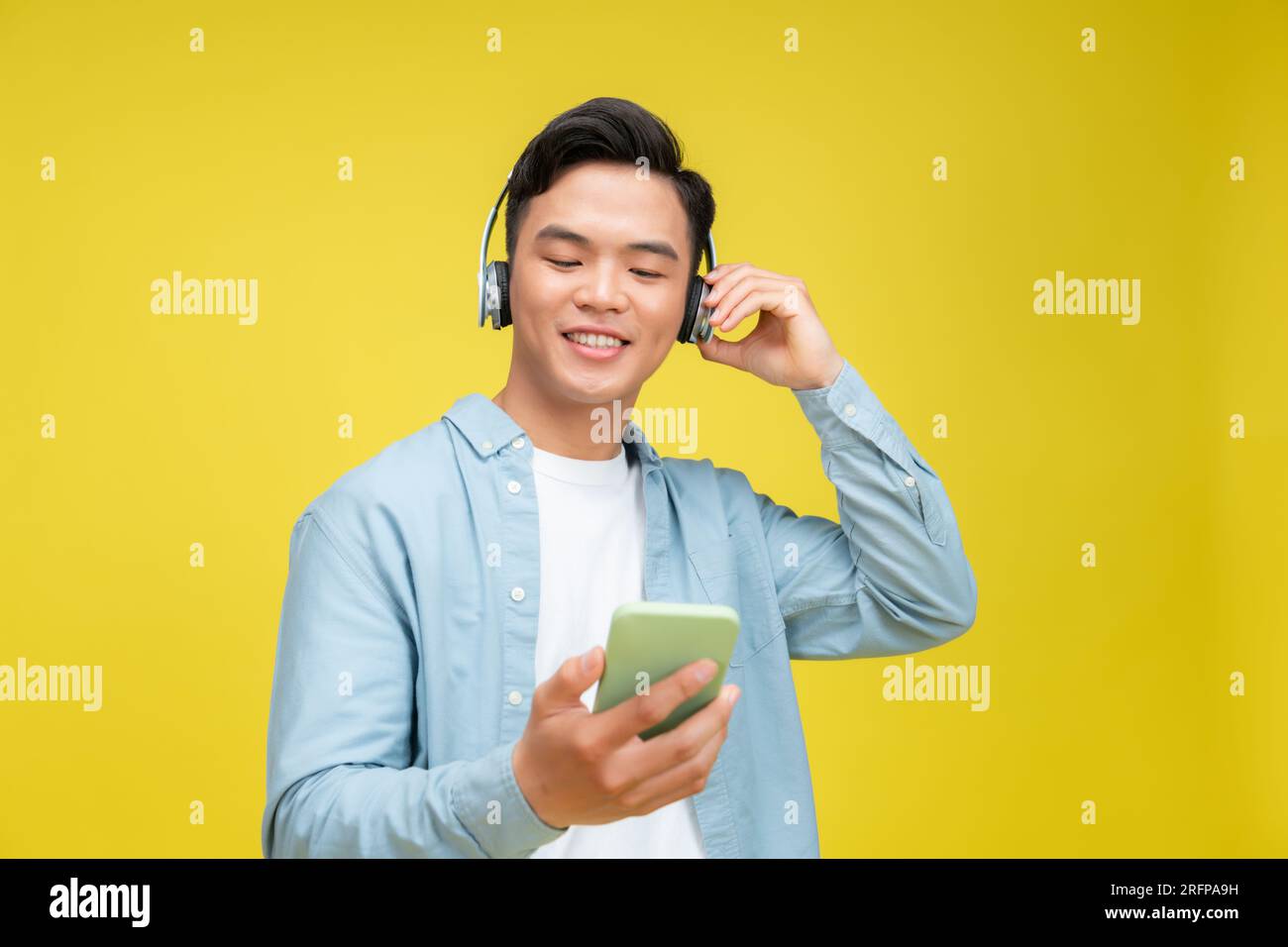 Delighted young Asian man wearing technology wireless headphones for listening to music via mobile phone Stock Photo