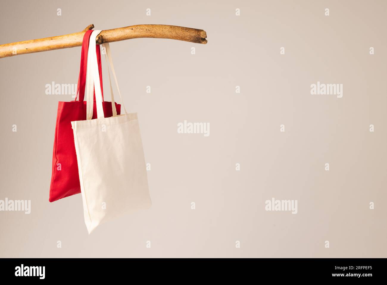 White and red canvas bags hanging from wooden branch with copy space on