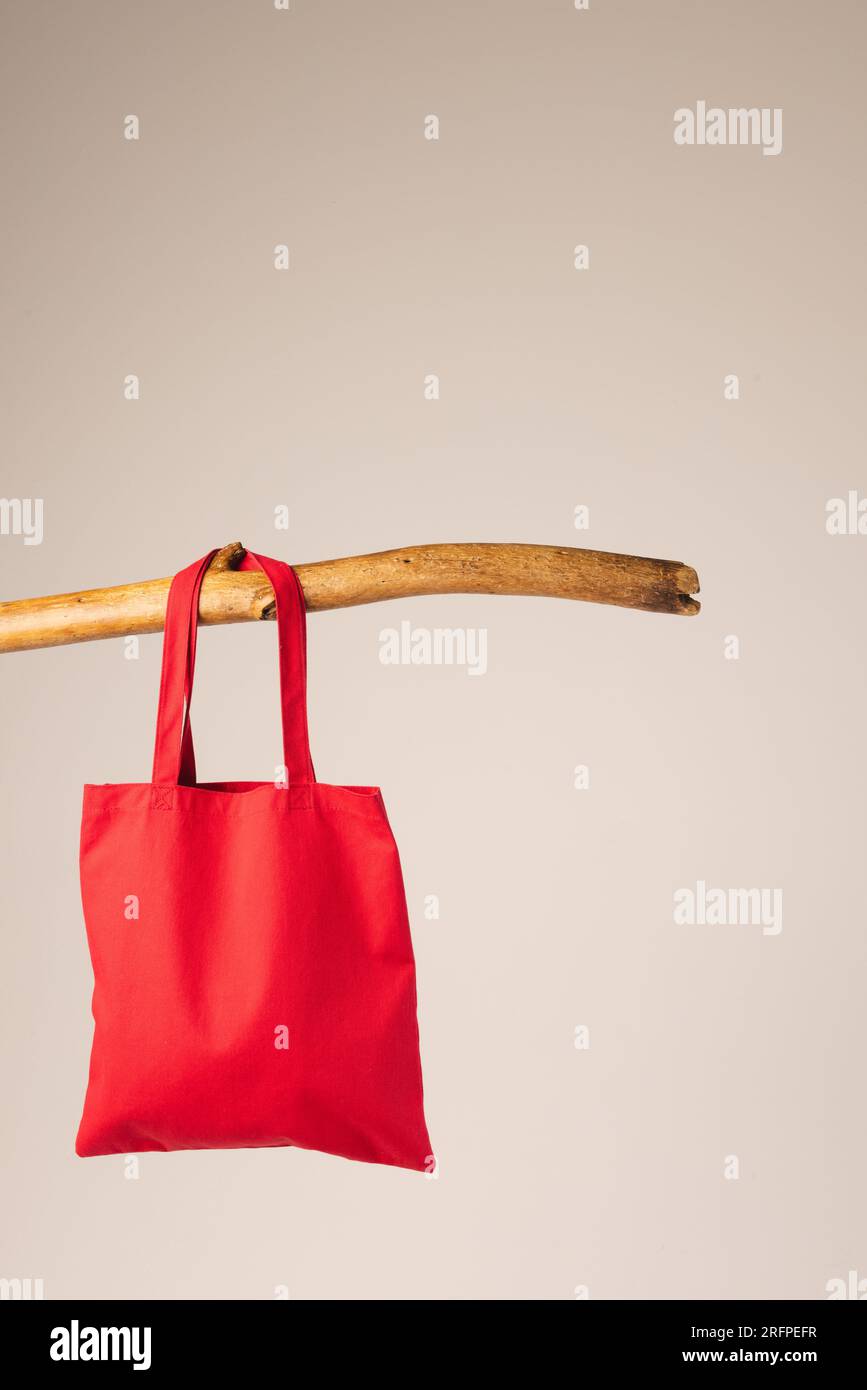 Red canvas bag hanging from wooden branch with copy space on white