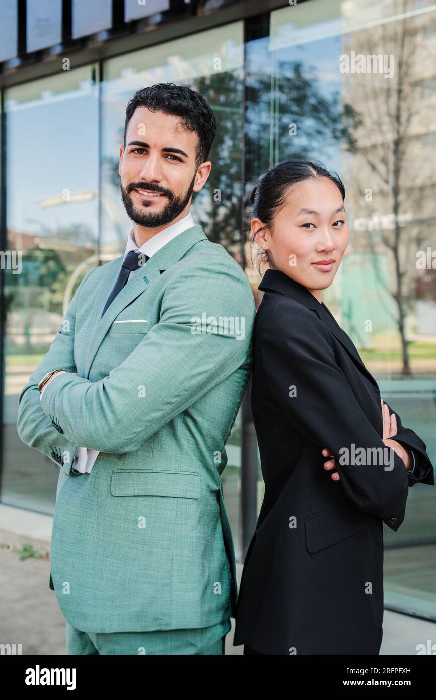 Vertical portrait of young arms crossed executive coworkers looking at camera at workplace buildings. Finance business people with successful expression. Couple of smart partners wearing formal suit. High quality photo Stock Photo