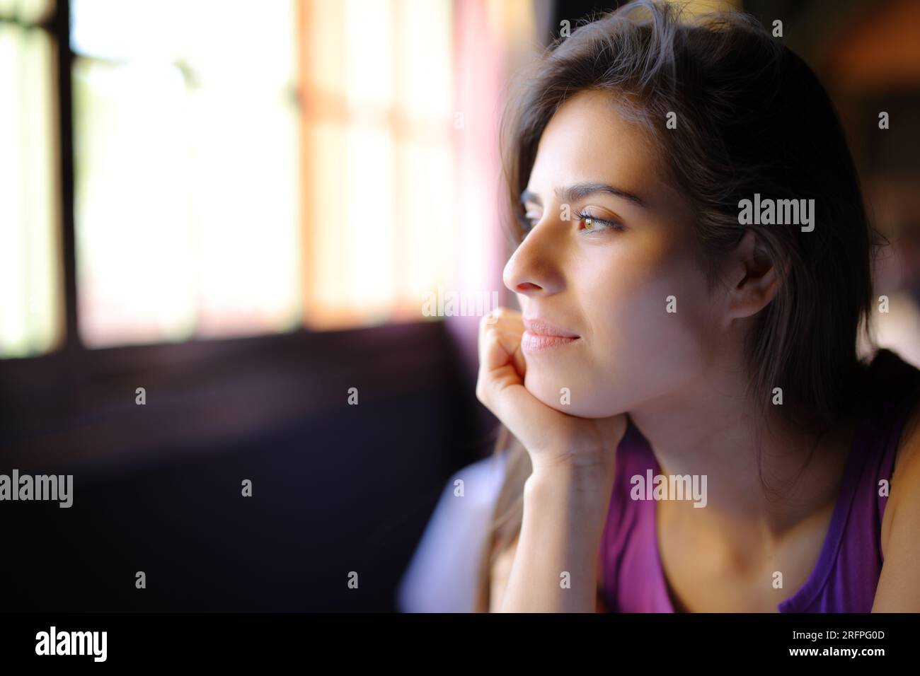Satisfied woman looks through a window at home Stock Photo