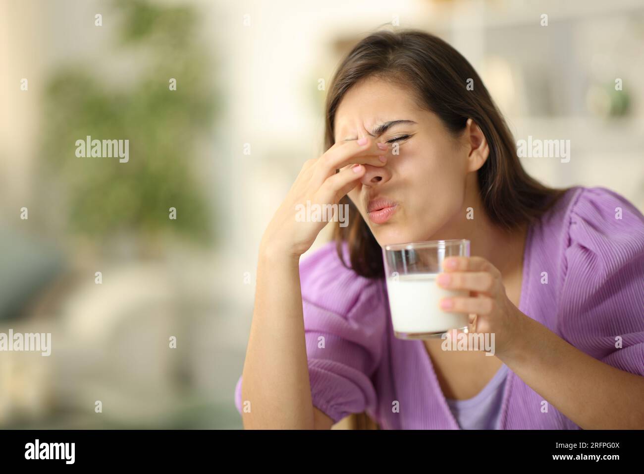 Woman smelling expired milk covering nose at home Stock Photo