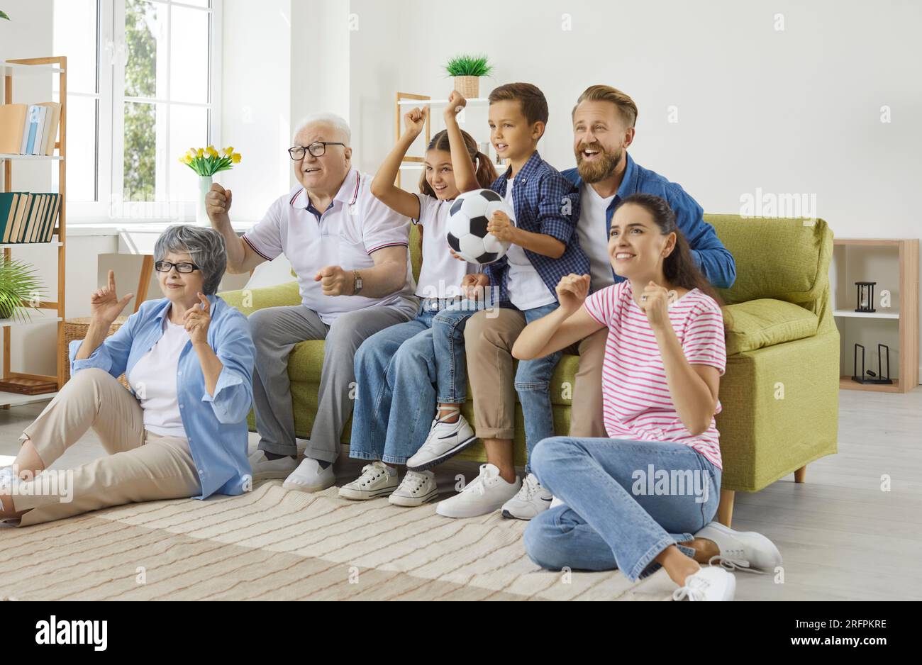 Family grandparents, parents and children football fans watching soccer game on TV. Stock Photo