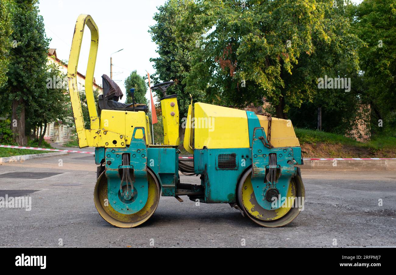 Steam roller standing idle on a path with an old stone wall and trees to the rear. road renovation, pavement patching repair Stock Photo