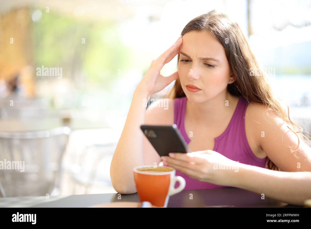 Worried woman checking phone sitting in a bar terrace Stock Photo