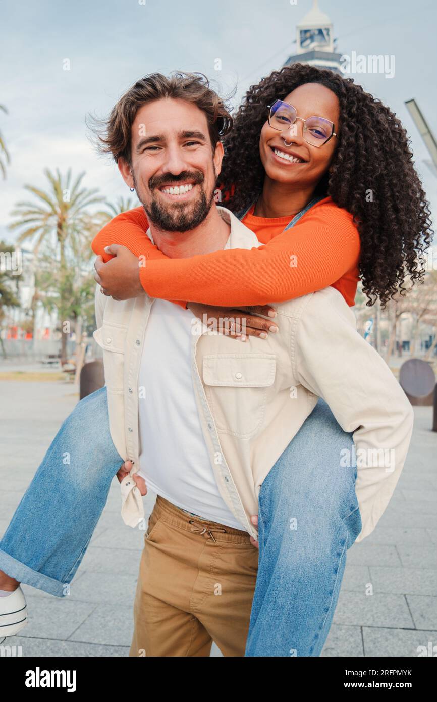 Verical portrait of couple embracing and having fun. Man giving his african american girlfriend a romantic piggyback ride enjoying a nice day together. Smiling guy in love carrying on back his woman. High quality photo Stock Photo