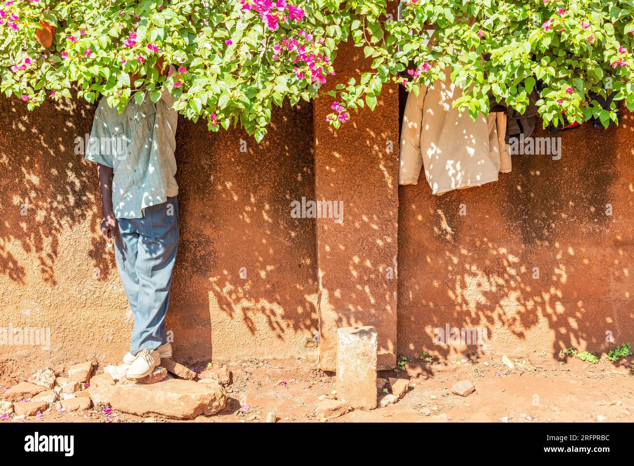 At the foot of an ocher wall, a man stands sheltered from the sun under ...