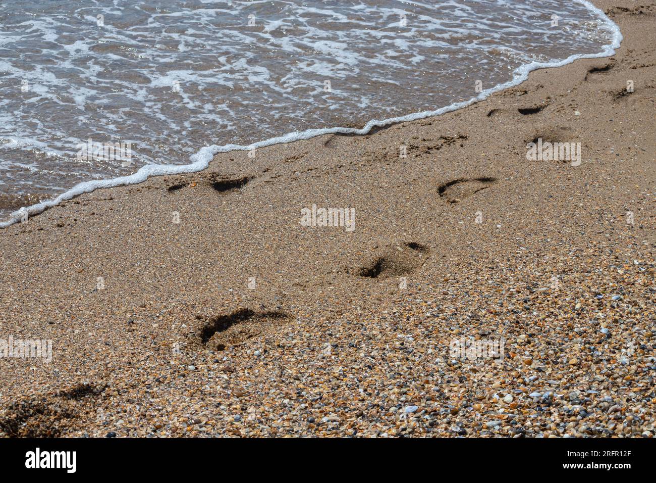 Footprints of a man on the yellow beach sand from walking barefoot by the sea with water that washes away the footprints. Contemplation of life Stock Photo