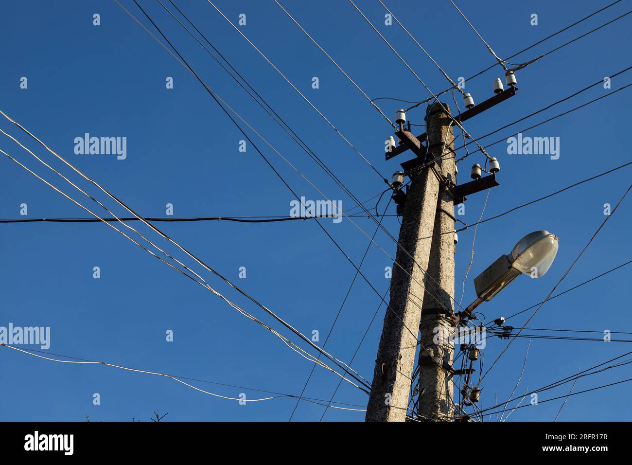 Electric wires hanging on a pole with a lighting lamp photographed from below on a background of blue sky. Stock Photo