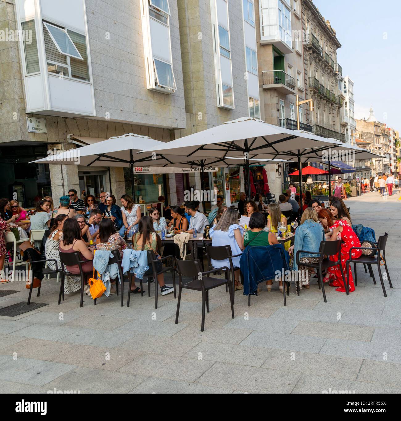 A large group of people sitting around  table at street cafe bar in the old town city centre of Vigo, Galicia, Spain Stock Photo