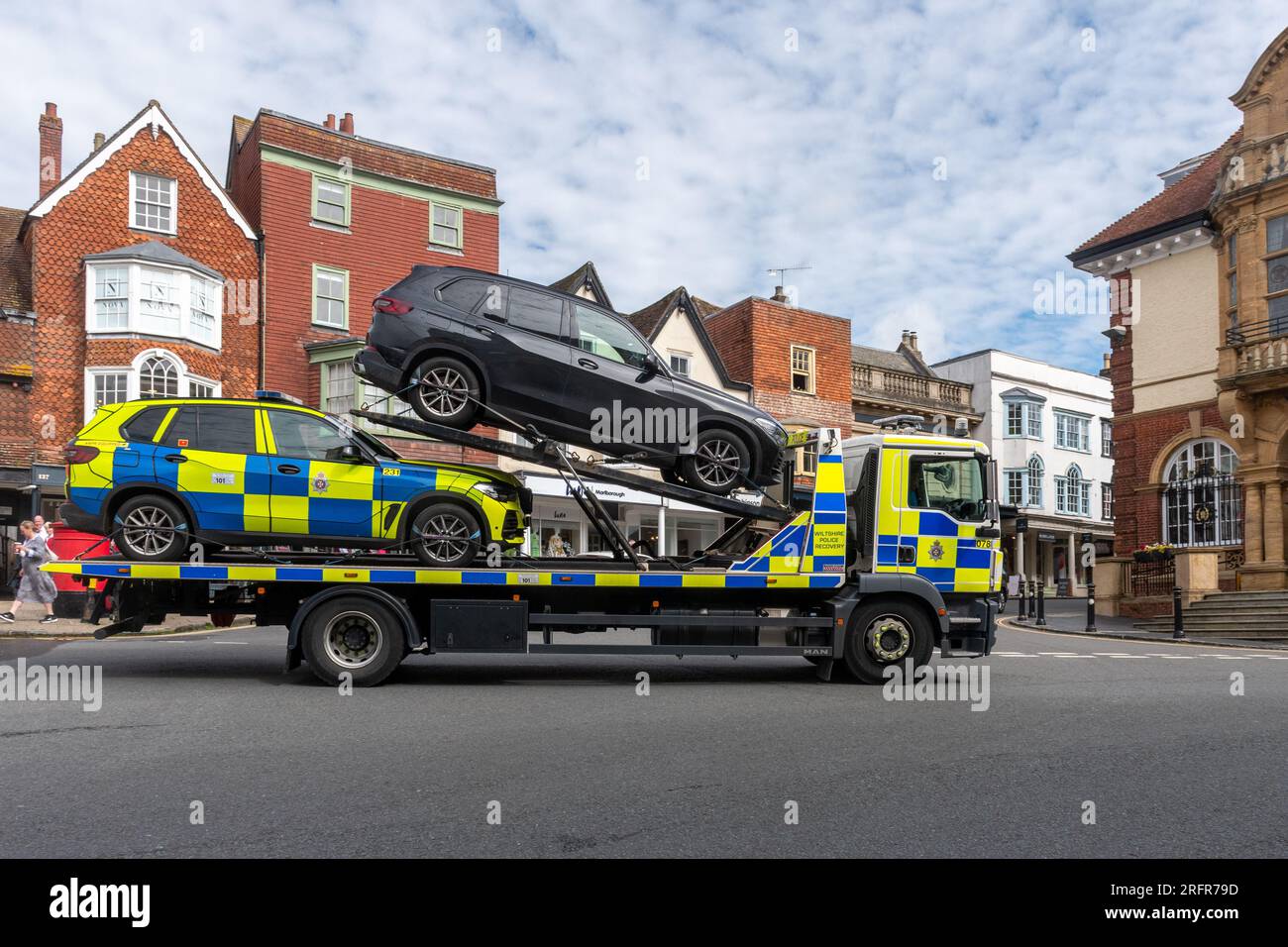 A police recovery vehicle lorry truck driving through Marlborough town centre, Wiltshire, England, UK, transporting an impounded car Stock Photo