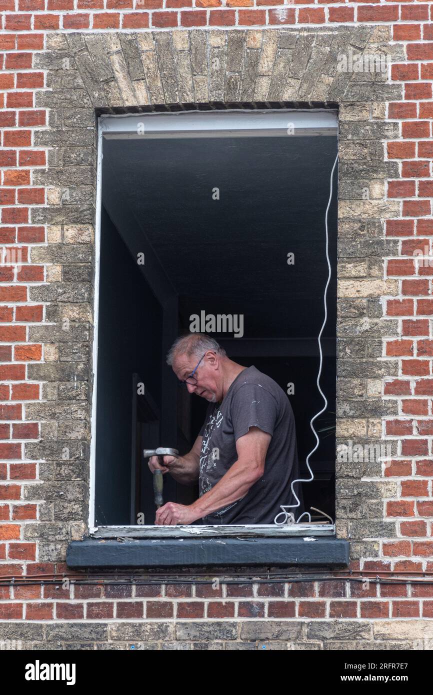 Window fitter at work working, removing old wooden window frame from a building, UK Stock Photo