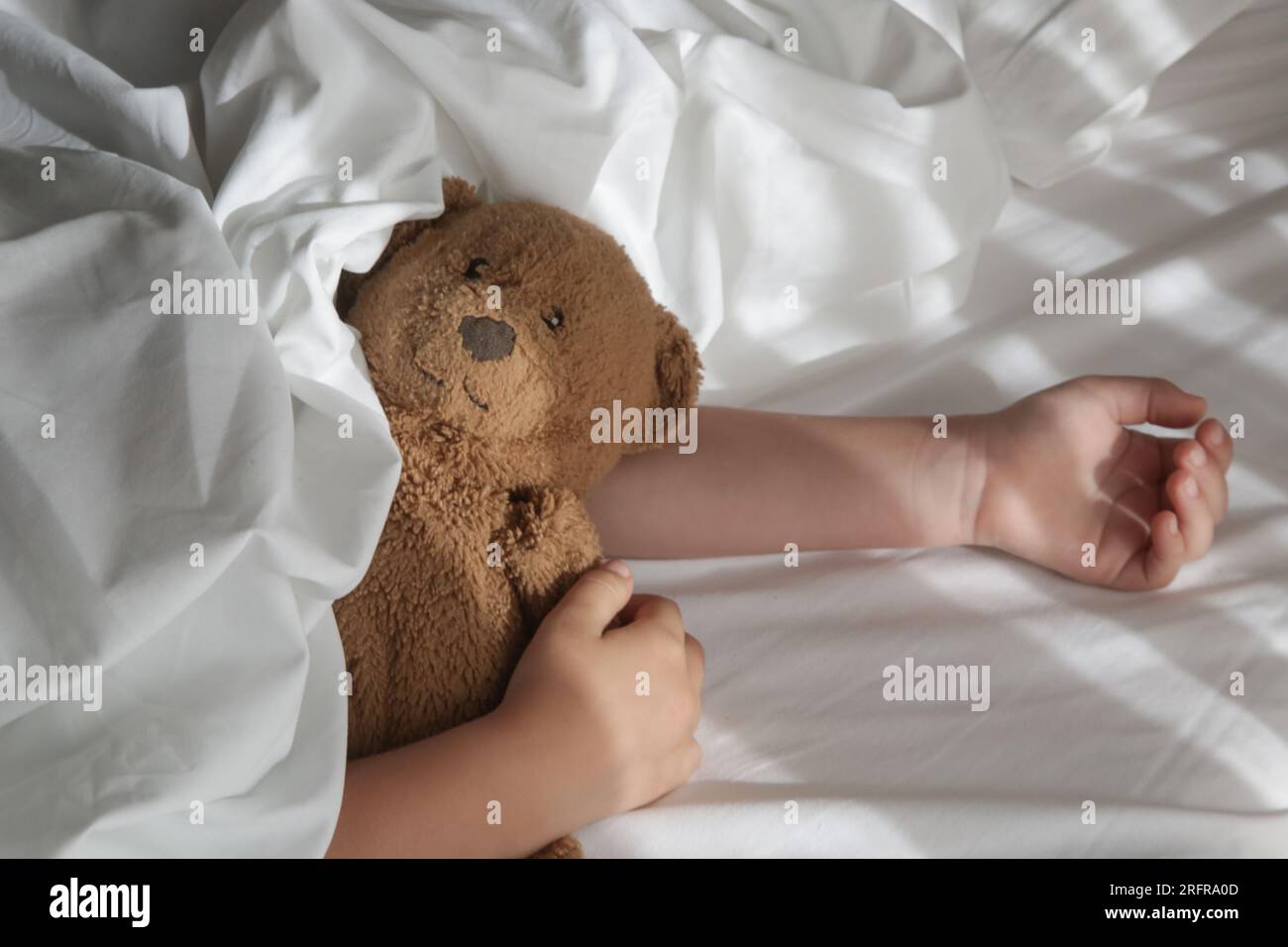 Child sleeping under white sheets hugging teddy bear. Children's nap time or bedtime Stock Photo
