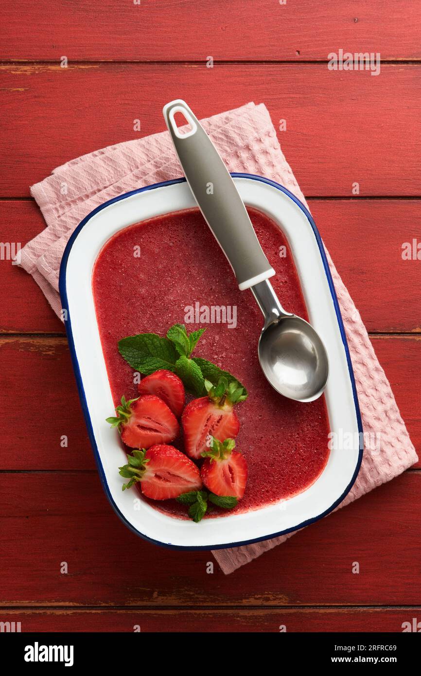Strawberry granita or fresh berry sorbet in white rustic bowl on old wooden table background. Ice cream with strawberry and mint. Summer treat. Top vi Stock Photo