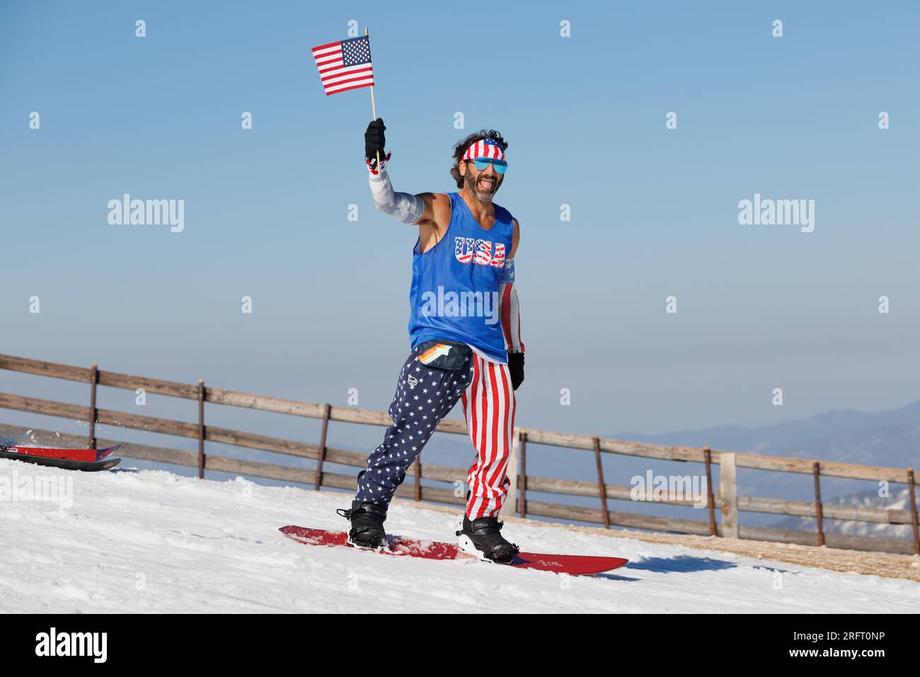 Mammoth Lakes, CA. July 4, 2023. A man in American flag pants and a USA tank top t-shirt waves an American flag while snowboarding at Mammoth Mountain Stock Photo