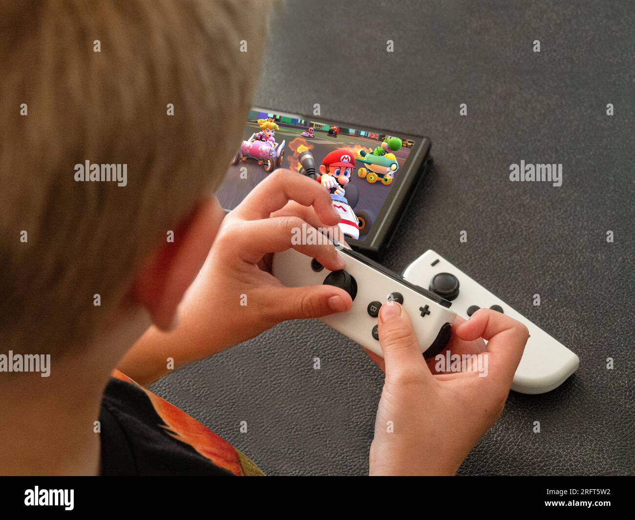 Young boy playing Mario Kart on a popular new Nintendo Switch console in handheld mode. Close up image on hands. Copenhagen, Denmark - August 5, 2023. Stock Photo