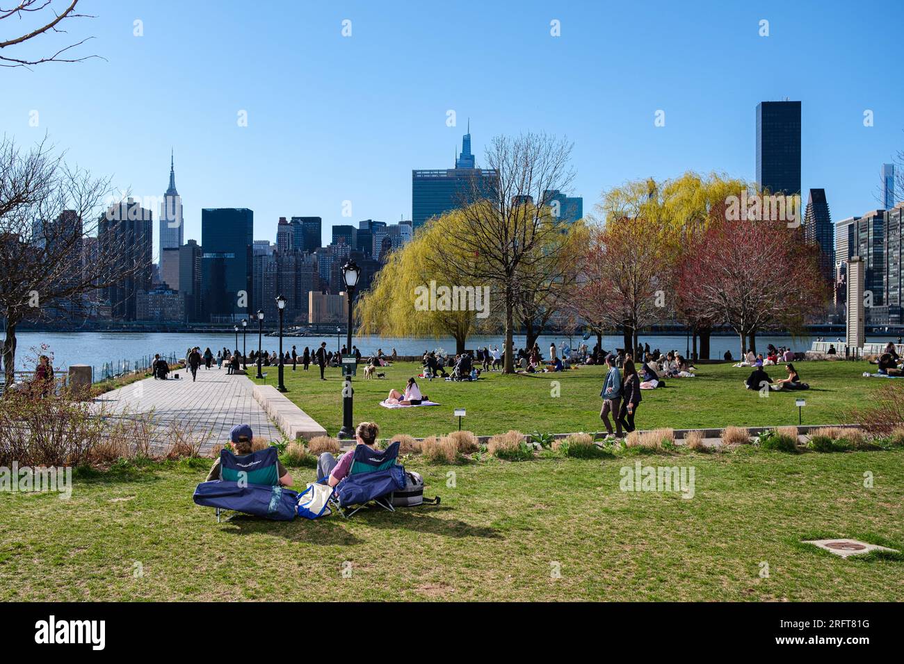 Sunlit park rendezvous overlooking Manhattan's skyline. A couple's embrace amidst blossoming spring, where nature frames their urban connection. Stock Photo
