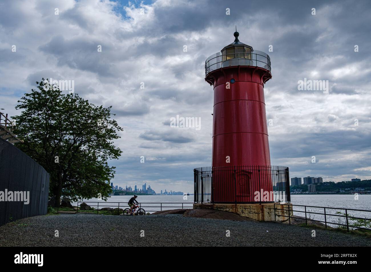 Cyclist's serene moment at Fort Washington Park, gazing upon Manhattan's skyline. A vibrant urban escape on a cloudy day. Stock Photo