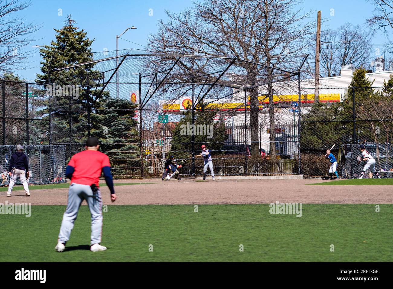 Amateur baseball under the sun in Forest Park, Queens. Springtime camaraderie as the batter connects. Vibrant outdoor play and community spirit captur Stock Photo