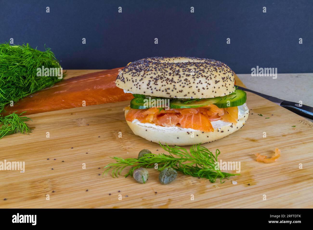 Seeded bagel with smoked salmon, cream cheese, cucumber, dill and capers on wooden board, landscape copyspace below. Stock Photo