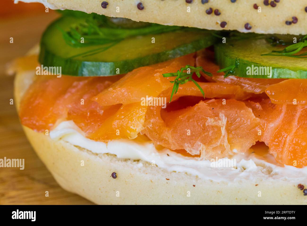 Seeded bagel with smoked salmon, cream cheese, cucumber, dill and capers on wooden board, landscape, macro. Stock Photo