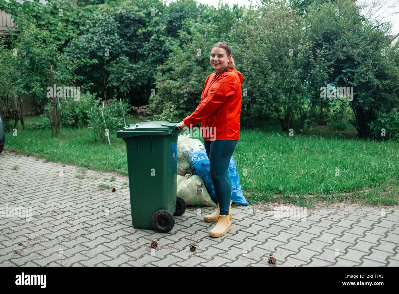 Adult woman household taking out bin to the street on rubbish day. Stock Photo