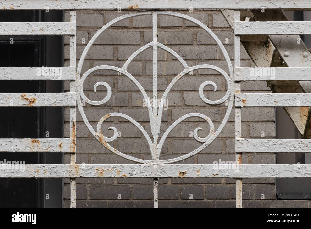 detail close up of wrought iron grate painted white on the side of fire escape with a decorative art deco medallion and peeling, rusting paint makes a Stock Photo