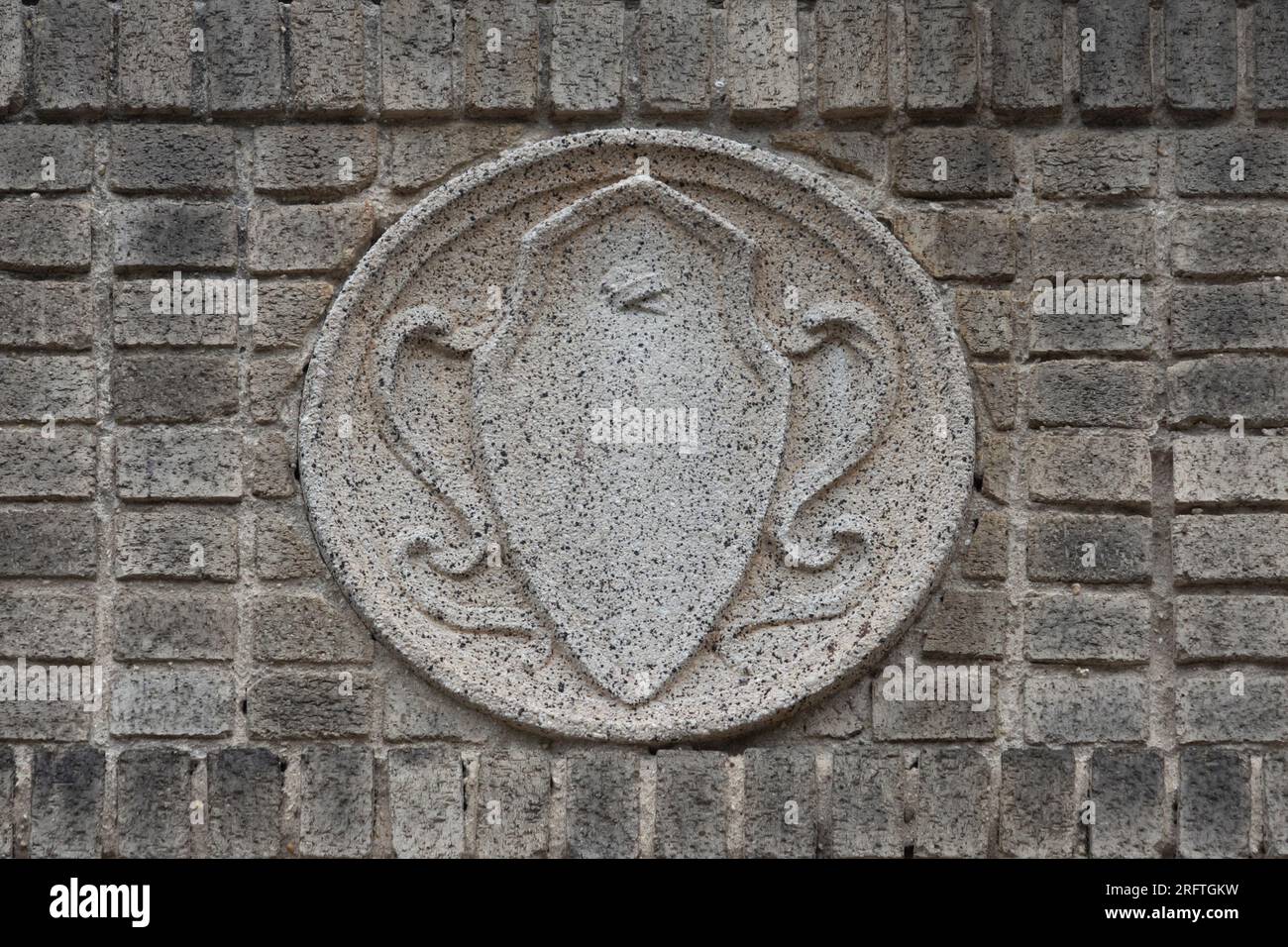 a molded concrete medallion in the art noveau style in neutral beige tones inset on a wall of beige gray bricks Stock Photo