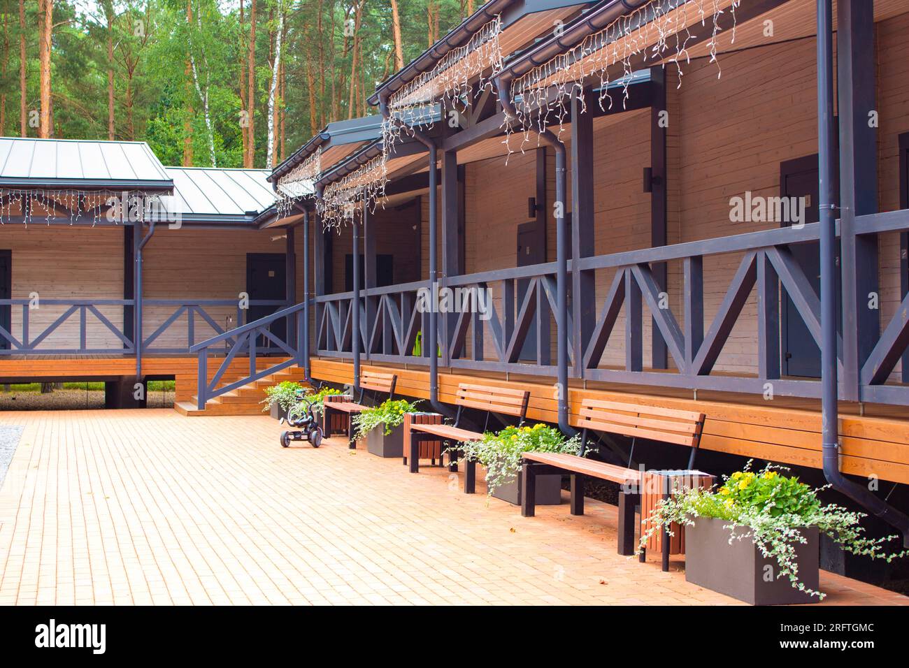 View of the hotel courtyard with outdoor terrace and benches. The wooden building of the hotel harmonizes with nature. Relaxation in nature. Stock Photo