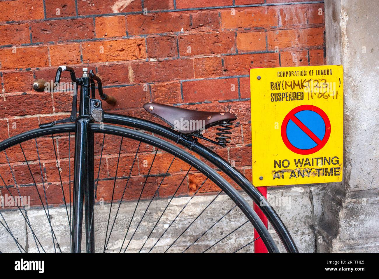 A penny farthing bicycle leaning against the wall with no Waiting at any time Sign. Stock Photo