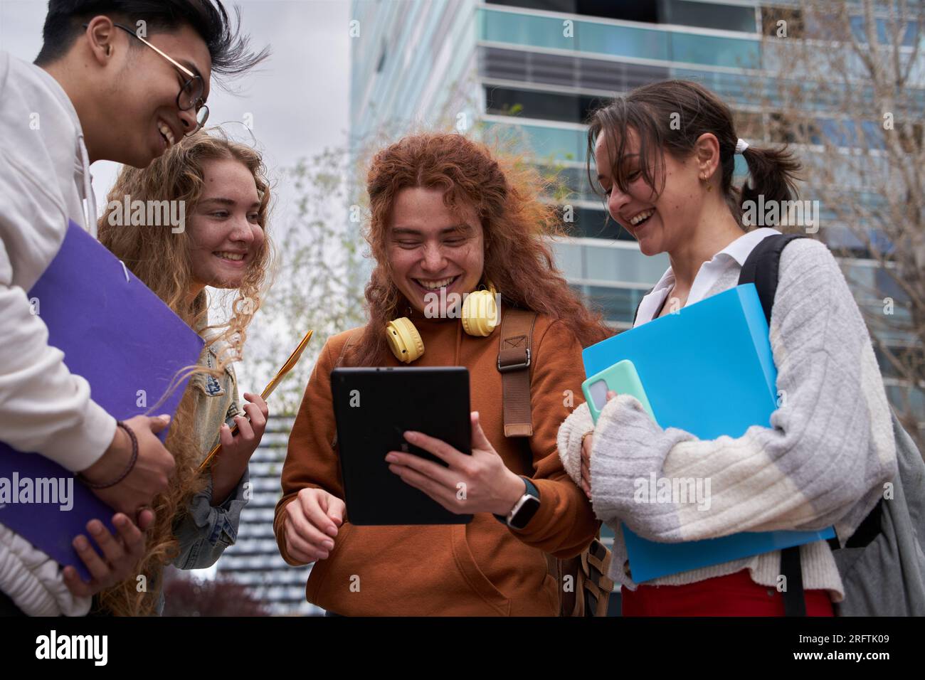 Group of students sharing an digital tablet to check internet standing up outside the campus Stock Photo