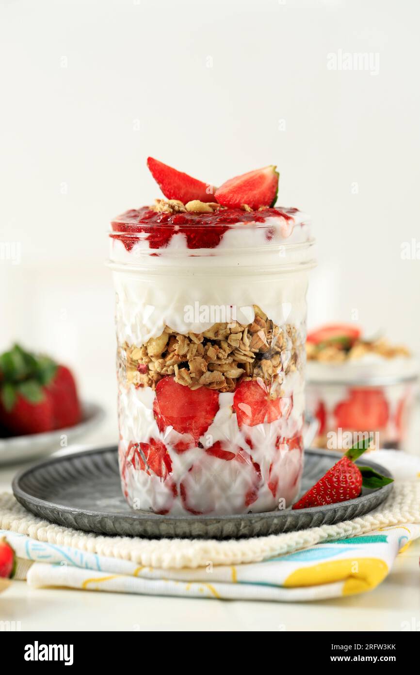 Strawberry Greek Yogurt Granola Parfait in a Drink Glass on White Table