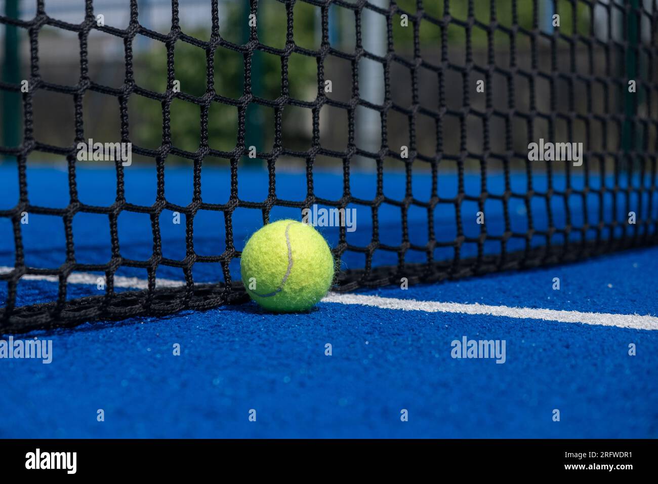 Yellow ball on floor behind paddle net in blue court outdoors. Padel tennis Stock Photo