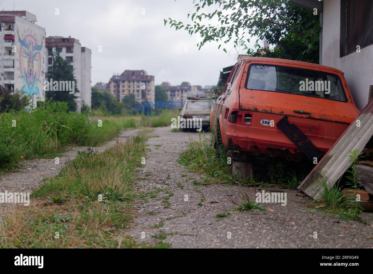 Dis-used cars parked in an overgrown area with street art on the side of apartment buildings in the capital city of Belgrade, Serbia. August 6, 2023. Stock Photo