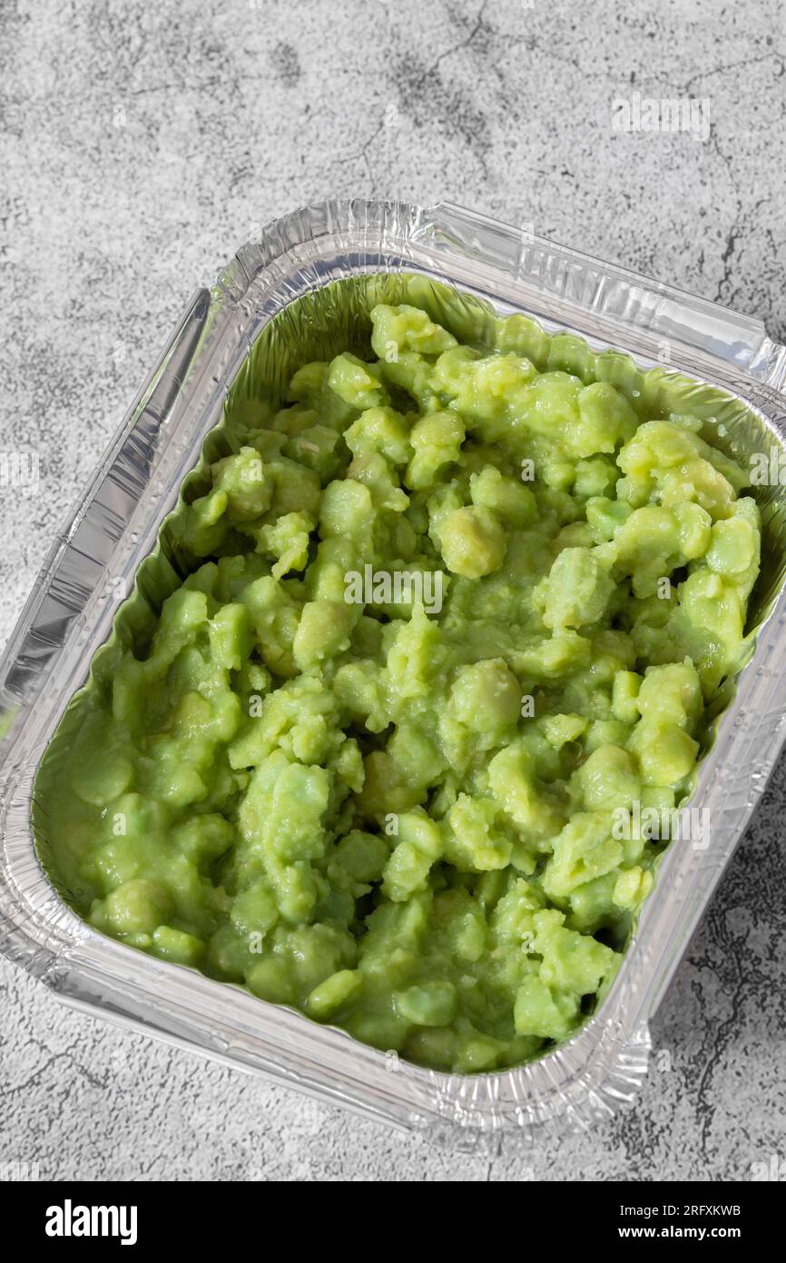Mushy peas in a takeaway foil tray carton container. On a concrete background Stock Photo