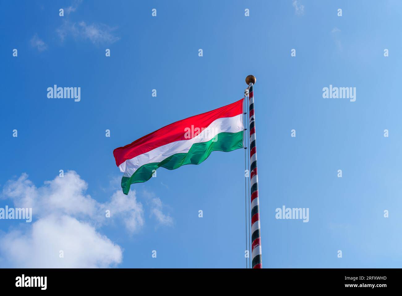 Hungary national flag waving on the wind on blue background. The flag of the Republic of Hungary is flying in the sky. Stock Photo