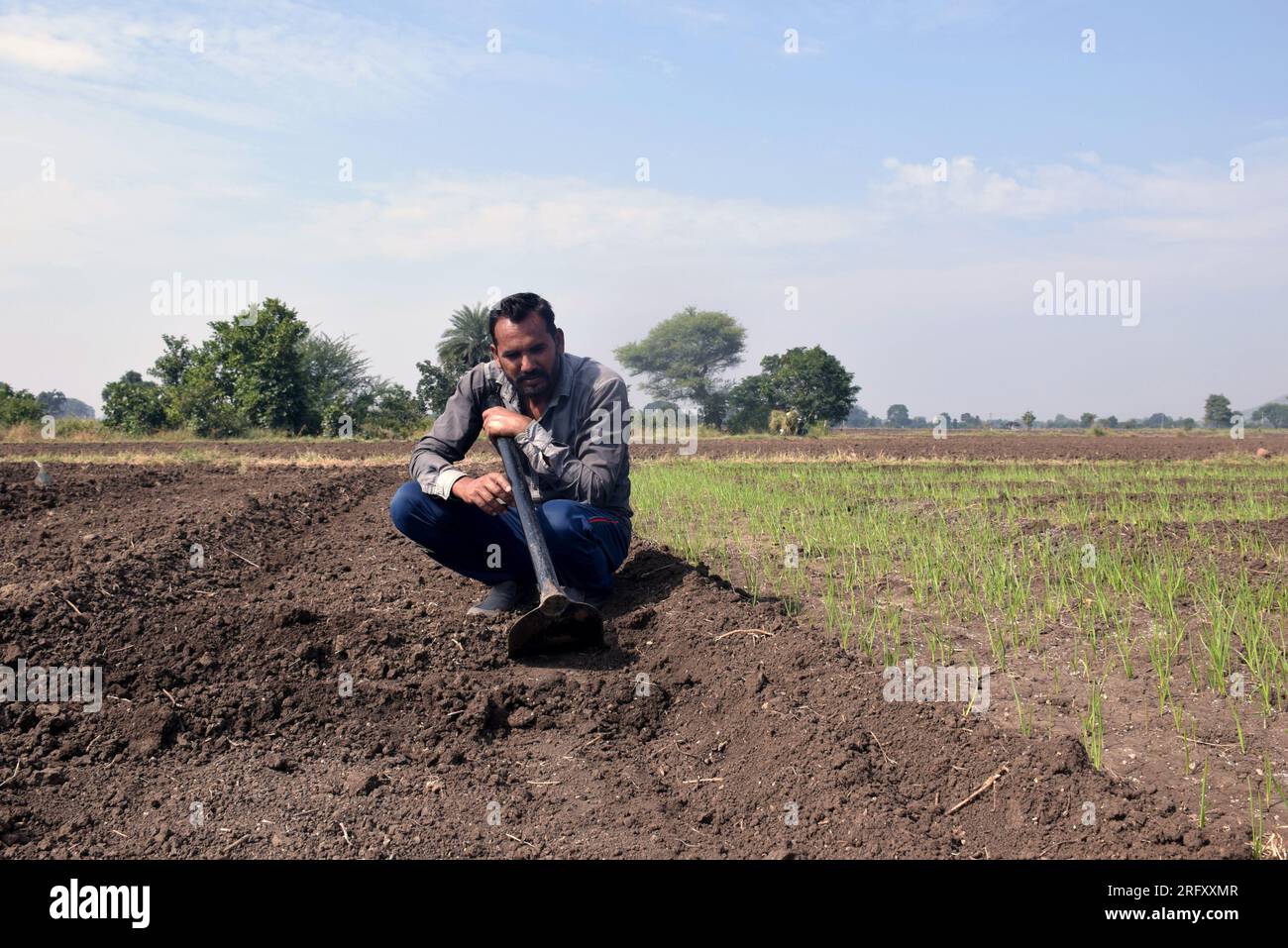 Indian farmer sitting in the field with a shovel, sluggish after ...