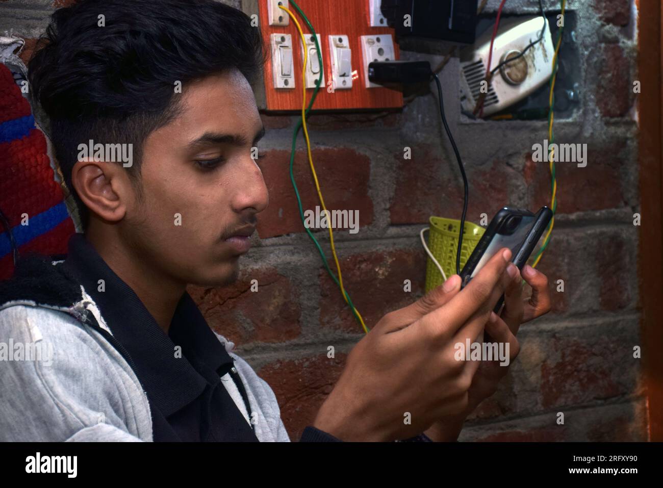 Indian teen using two mobiles simultaneously at home. brick wall and electric board background Stock Photo