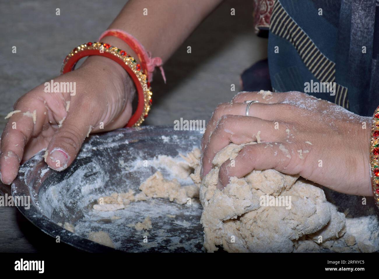 Indian woman hand in dough close-up kneading dough on steel plate, bangles hands Stock Photo