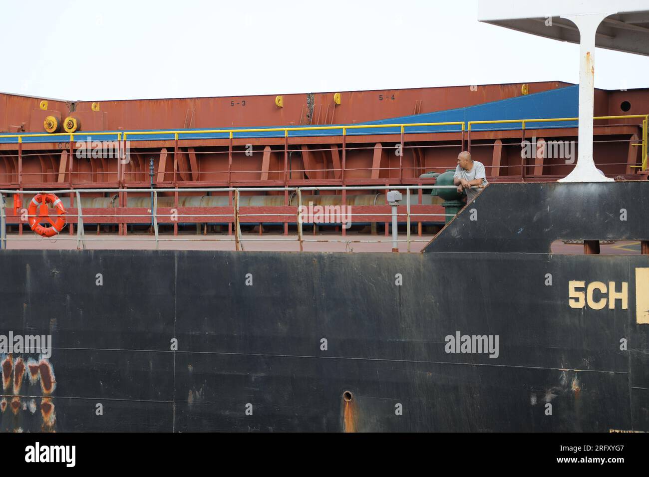 Sailorman leaning on the railing of a big ship, looking sidewards Stock