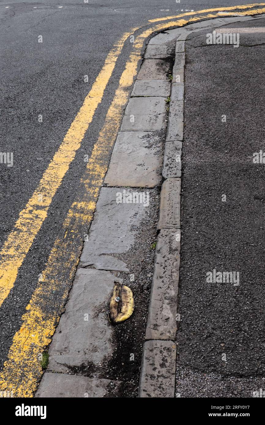 A banana peel lies on a roadside next to double yellow parking lines. Stock Photo