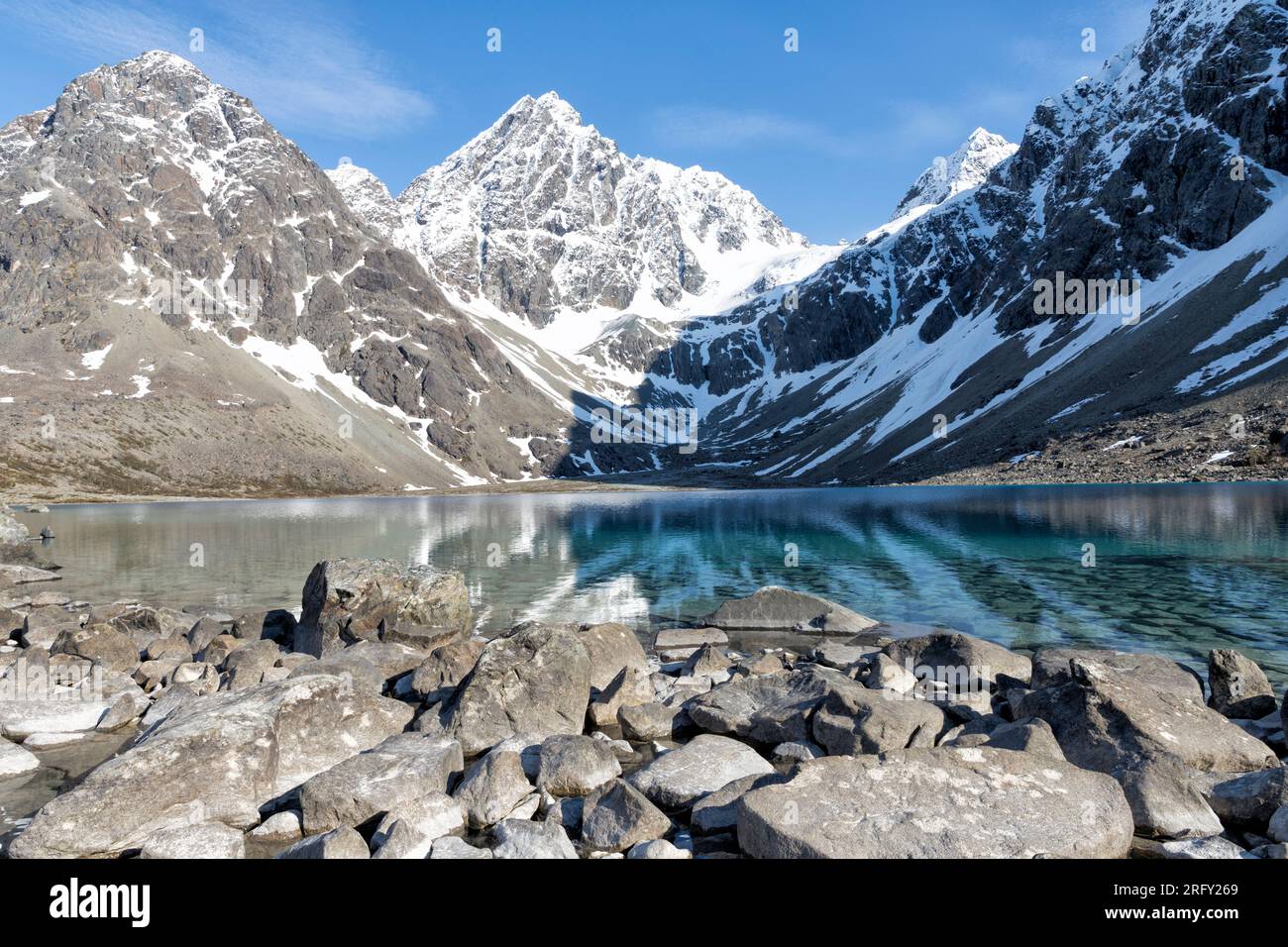 The surrounding, steep, snow-capped mountains are reflected in the intense blue water of Blåisvatnet. Lyngen Alps, Troms and Finnmark, Northern Norway Stock Photo