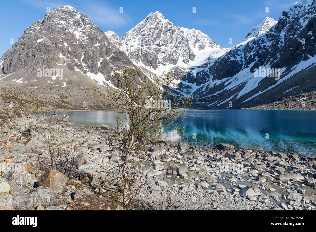 The surrounding, steep, snow-capped mountains are reflected in the intense blue water of Blåisvatnet. Lyngen Alps, Troms og Finnmark, Northern Norway Stock Photo
