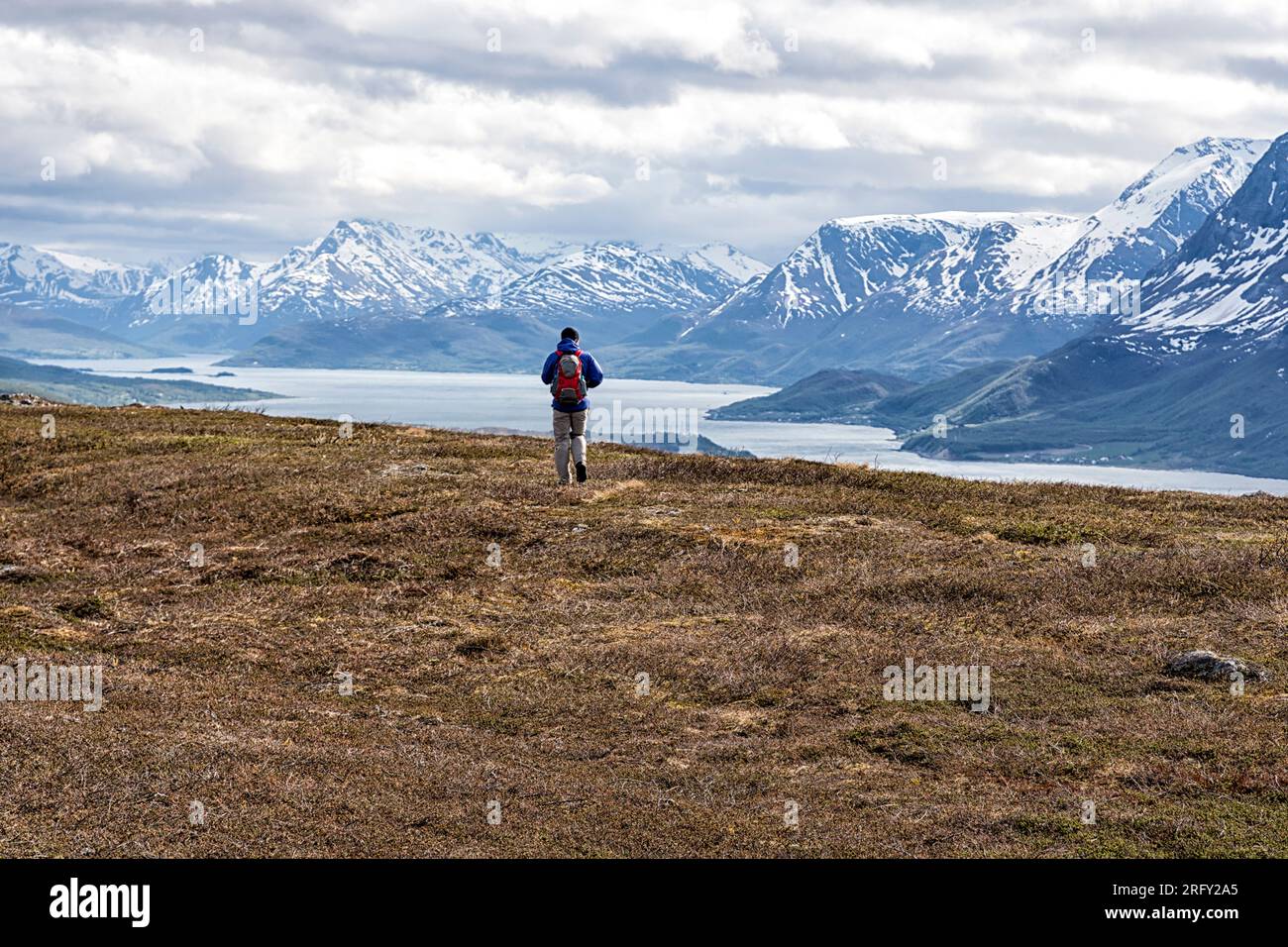 A man is hiking on the summit of Barheia. Panoramic views of the fjord and snow-capped mountains. Svensby, Lyngen Alps, Lyngsalpan, Northern Norway Stock Photo