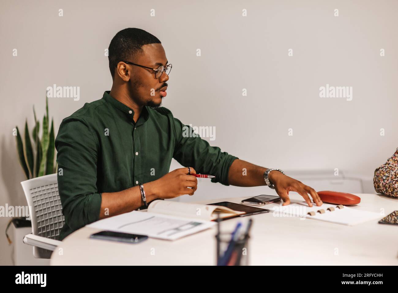 Multi-tasking businessman working at modern office. He is using tablet, financial reports, notebooks Stock Photo