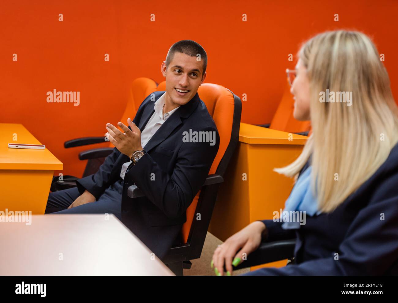 Two young and well-dressed students talking and smiling while attending a lecture Stock Photo